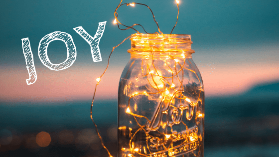 The word JOY against a colorful background with a jar of tiny lights